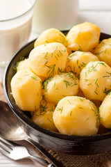 Boiled potatoes with dill in bowl on white wooden background.