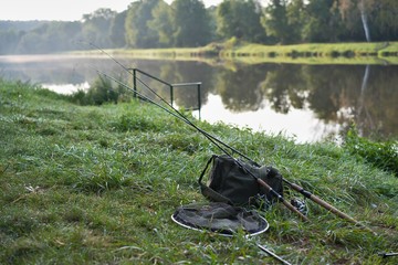 Obraz na płótnie Canvas Early morning by the biggest river in Czec Republic named Elbe, fishing tackle consist from fishing rod, dip net and bag with spinners and lures waiting for angler. Nice nature, sport and vacation. 