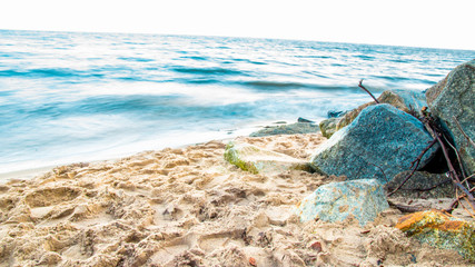 Fototapeta na wymiar Piaszczysty brzeg morza z kamieniami leżącymi na plaży, rozmyte fale na morzu bałtyckim