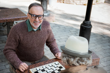 Cheerful mature man playing draughts with comrade