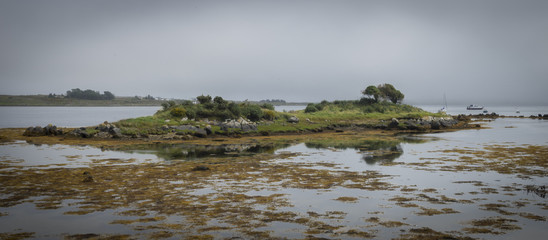 Panoramique, pose longue d'un Îlot sur la côte avec reflet sur l'eau, rochers et algues 