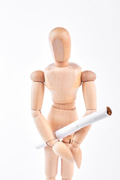 Wooden dummy with white cigarette. Human wooden mannequin holding cigarette with filter over white background.