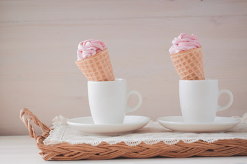 Pink marshmallows or zephyr in white cups on the wooden background