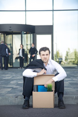 Fired businessman sitting on street