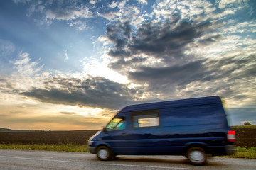 Fototapeta na wymiar Delivery van on a country road. Asphalt road, journey to the Sunset