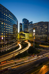 Fototapeta premium Skyscrapers in Paris business district La Defense. European night cityscape with dynamic street traffic, car lights and glass facades of modern buildings. Economy, finances, transport concept. Toned