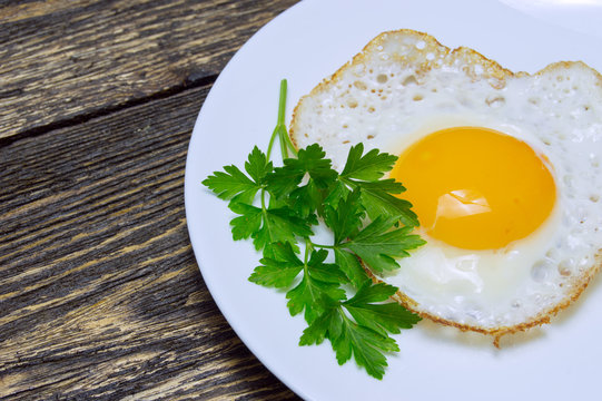 Fried egg with green parsley on plate close up, on vintage wooden background