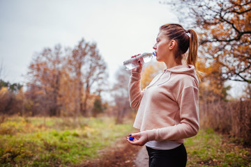 Fototapeta premium Woman runner drinks water in autumn forest