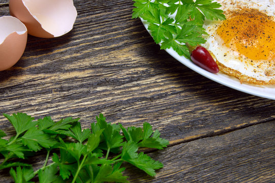 Fried egg with spices, green parsley on plate with pepper and eggshell, on vintage wooden background