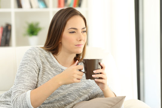 Pensive girl holding a cup of coffee on a sofa at home