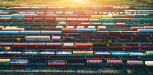Top view of cargo trains. Aerial view from flying drone of colorful freight trains on the railway station. Wagons with goods on railroad. Heavy industry. Industrial conceptual scene with trains. - obrazy, fototapety, plakaty