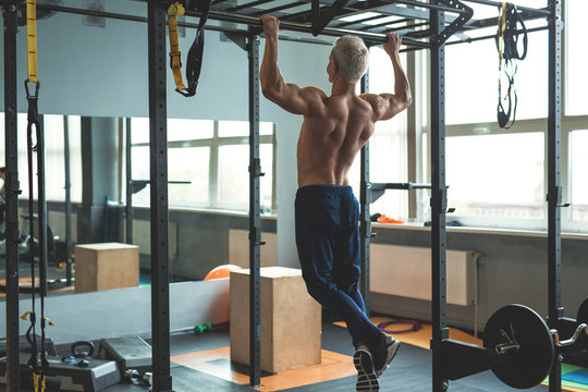 Muscular athlete man making Pull-up in gym. Bodybuilder training in fitness club showing his perfect back and shoulder muscles. Toned image