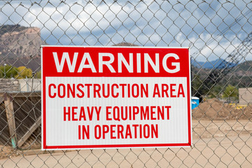 Warning construction area sign hanging on a chain link fence