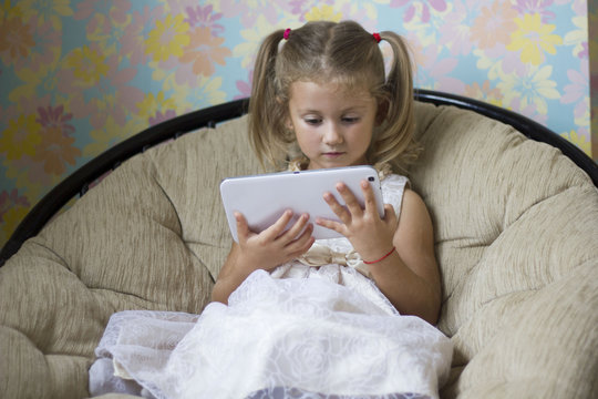 little girl in beautiful dress sitting in a chair with a tablet in hand