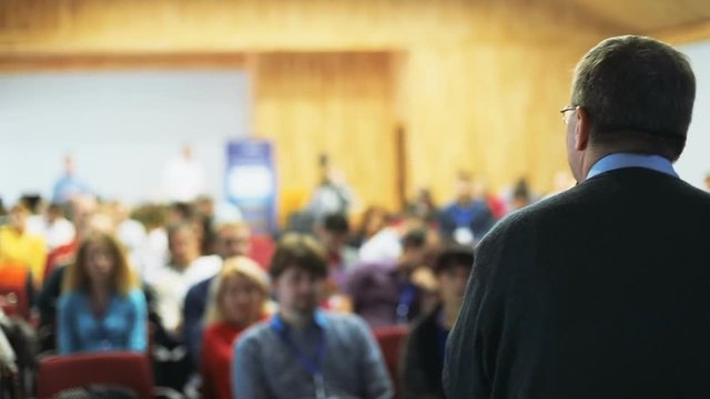 talking adult intelligent man back view talking microphone speaking holding mike audience public space conference hall convention center education lecture students blurred people listeners background