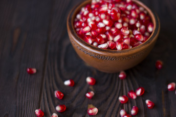 ruby pomegranate seeds in a clay bowl on wooden table