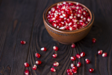 ruby pomegranate seeds in a clay bowl on wooden table