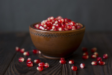 ruby pomegranate seeds in a clay bowl on wooden table