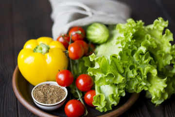 fresh organic vegetables: tomatoes, peppers, cucumber, chili, spices and salad in a clay plate on the table dark wood