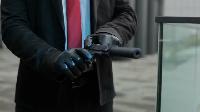 Hands load a pistol with a silencer, these are the hands of a hired killer.