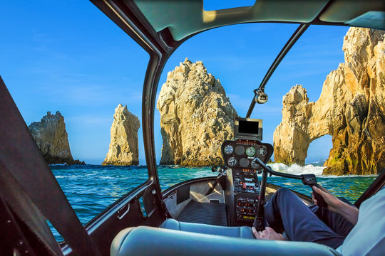 Fight view of Los Arcos rock formation at Lands End in Cabo San Lucas, Baja California Sur, Mexico. Helicopter cockpit with pilot arm and control console inside the cabin. Summer and holidays concept.