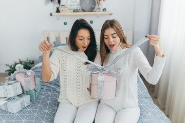 Two happy, stylish and beautiful girl friends presented each other with Christmas gifts and opened them up in the vintage white room.