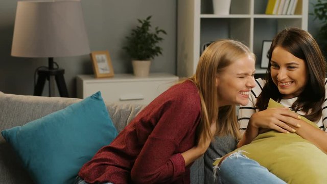 Two pretty young women telling secrets and gossiping in the cosy living room. Whispering. Indoor