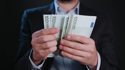 A man wearing a black jacket and a white shirt holding cash (Euros) against a black background. Close-up shot - Powered by Adobe