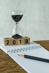 new year 2018 goals, target or checklist concept as number 2018 wooden cube block with sandglass and white paper note with pencil on wooden table
