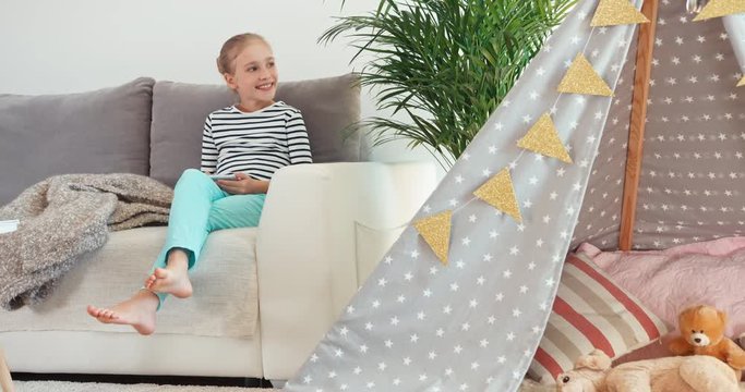 Child girl using cell phone sitting on the sofa