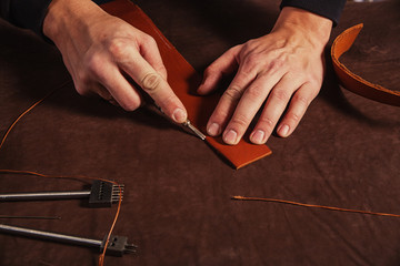 A close-up of a skinner man makes a genuine leather belt, cuts the skin with a special knife on the...