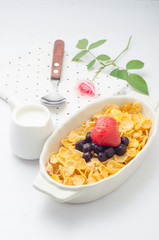 Cornflakes cereal and fruit in white bowl with mill on wooden table.