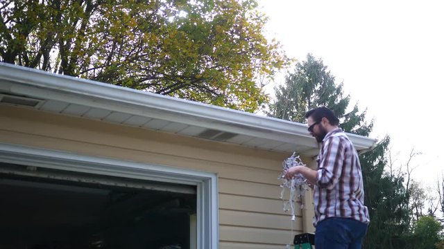 Caucasian Millennial Husband Frustrated At Hanging Icicle Lights For Christmas Time On Ladder