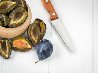 Sliced halved plums in a wooden bowl on a white table top view.