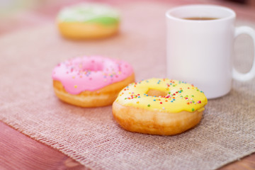 Donuts with icing on the table. Nearby is a mug with coffee. Sweet colored donuts