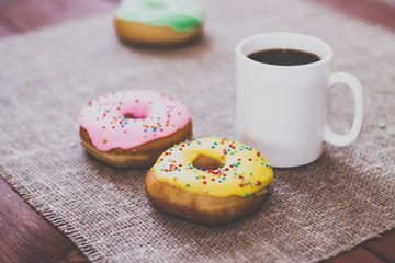 Donuts with icing on the table. Nearby is a mug with coffee. Sweet colored donuts