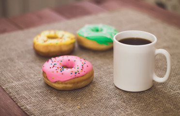 Donuts with icing on the table. Nearby is a mug with coffee. Sweet colored donuts