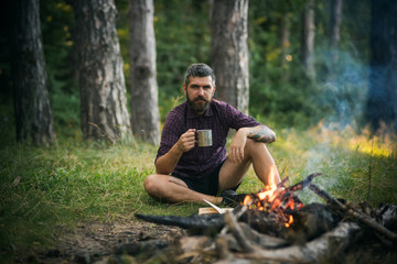 Naklejka na ściany i meble Hipster hiker with mug relax at bonfire in forest