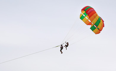 People are enjoy parasailing water sport. Fly with colorful parachute on the sky over the beach.