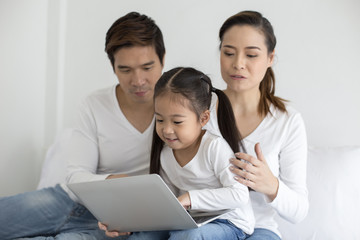 Attractive Little Girl using Laptop with Mom and Dad Together. Girl learning to use Laptop. Happy Family Concept.