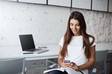 Young happy beautiful lady using a smart phone to learn new language in a bright cafe. Education concept.