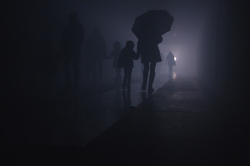 silhouette of a woman with a child walking under an umbrella in a tunnel