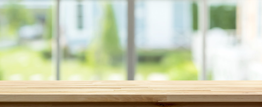 Wood table top inside the house with blur green garden outside window in background, panoramic banner