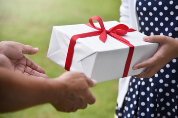 Asian woman giving a white gift box to elderly man.