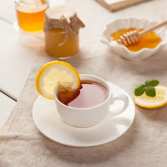 Closeup of cup of tea with lemon, mint on white wooden background. Black herbal tea with lemon, ginger and honey. hot winter drink