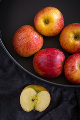 Red apples in a black bowl on a Black fabric background