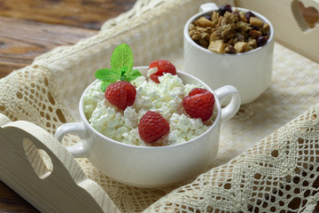 Homemade breakfast: cottage cheese with fresh raspberries and granola. In a white porcelain bowl, on a wooden tray