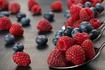 full spoon with blue-berries and raspberries on a dark background
