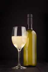 Green bottle of white wine and wine glass mock up on elegant dark black wooden background, vertical. 