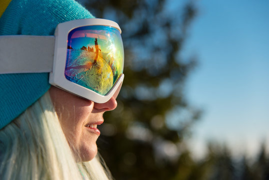 Close-up profile shot of a smiling female snowboarder wearing skiing mask, looking away, resting in the mountains on a sunny beautiful day copyspace sports activity recreation active lifestyle
